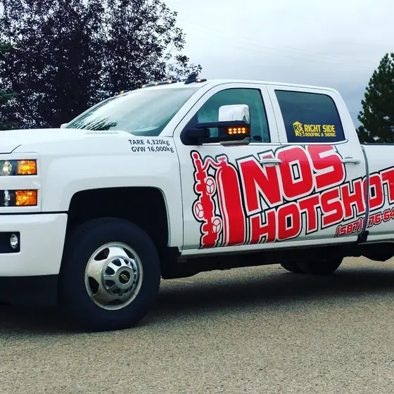 White NOS Hotshot dually pickup in full wrap, parked side-on with the red wellhead logo across the door and box