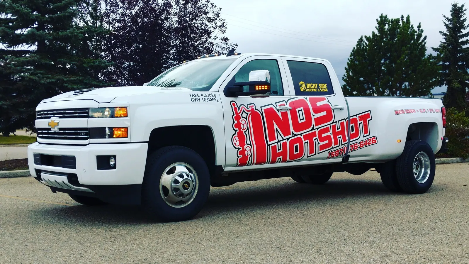 White NOS Hotshot dually pickup in full wrap, parked side-on with the red wellhead logo across the door and box